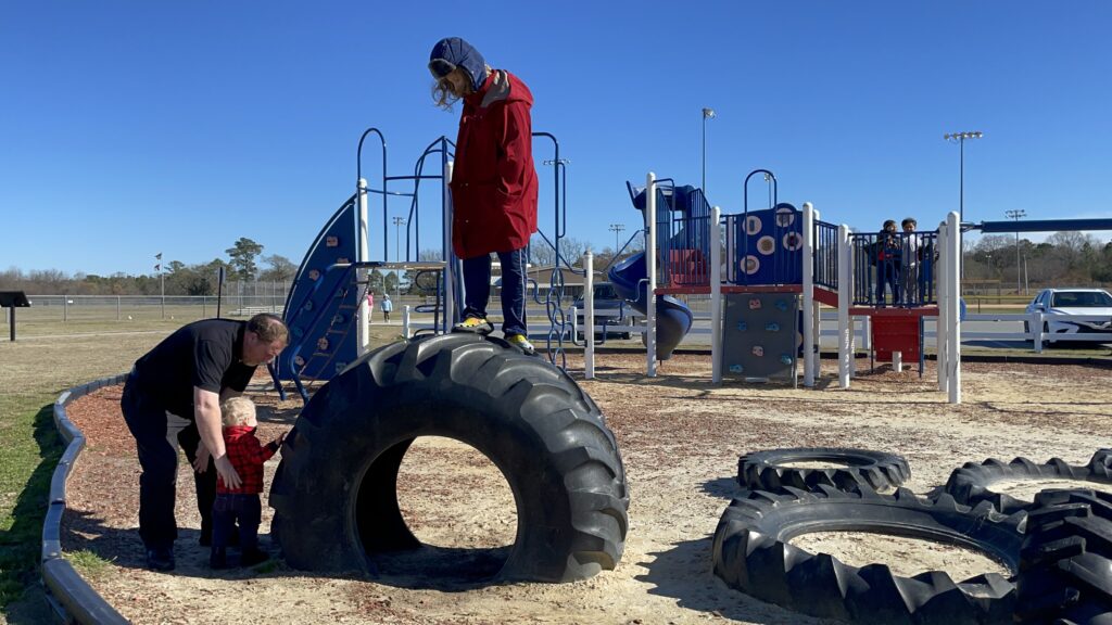Old playground layout. My husband helps the toddler while the oldest stands on a tractor tire with the old playground equipment in the background. 